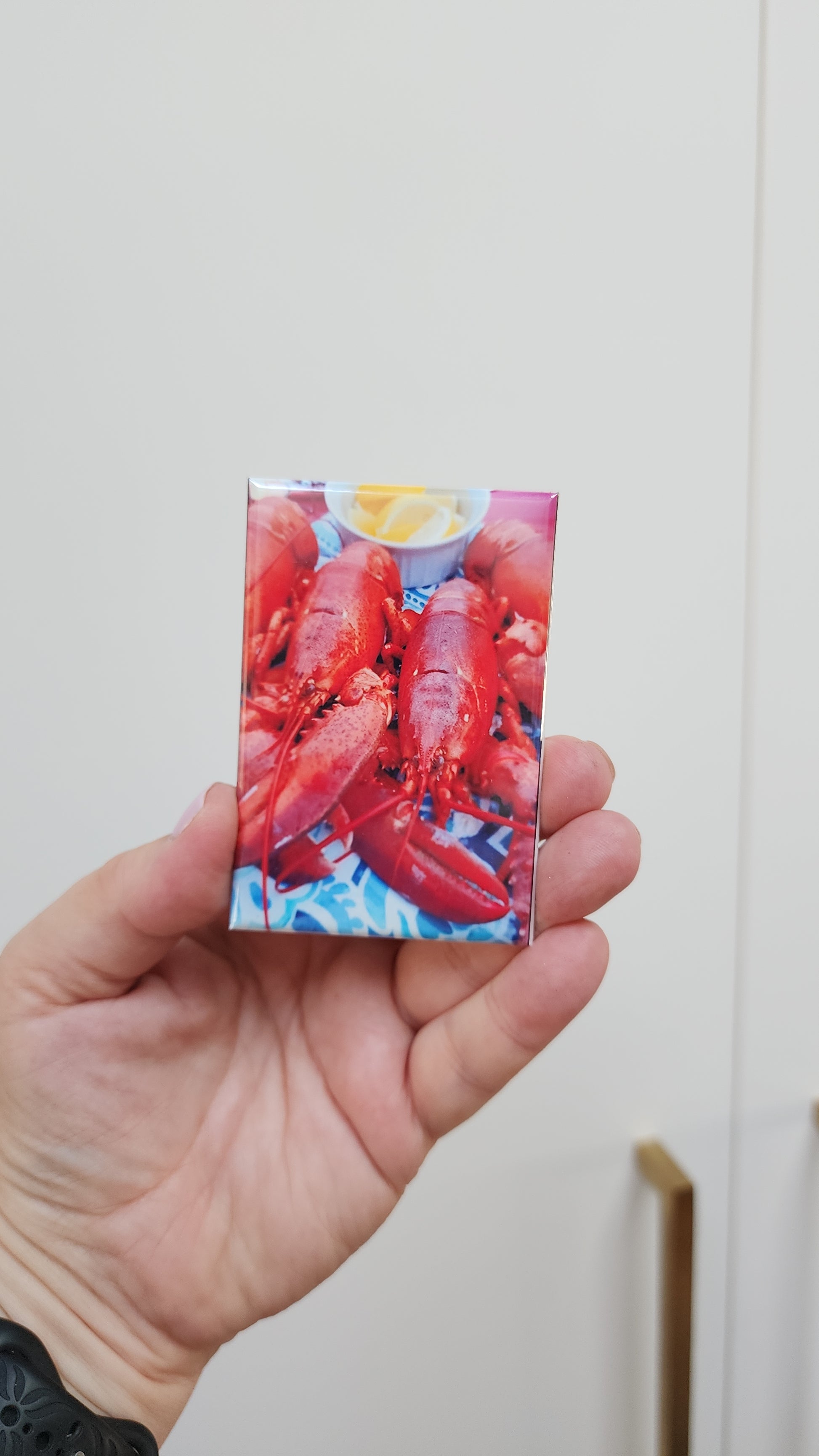 Hand holding a card with a lobster and lemon design against a white background