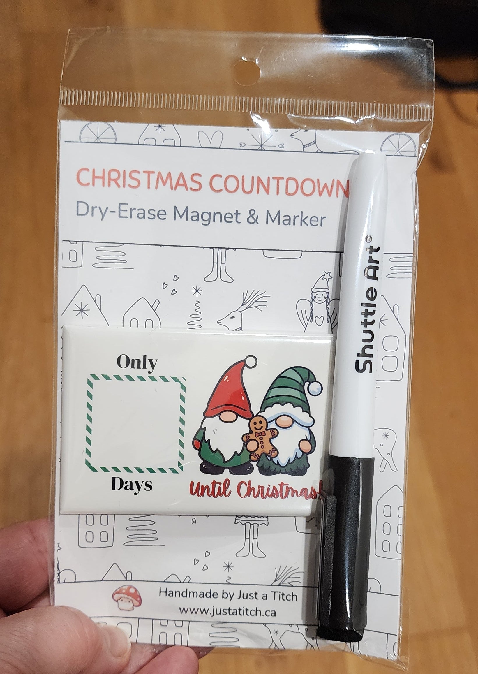 Hand holding a Christmas countdown magnet and marker set on a wooden surface